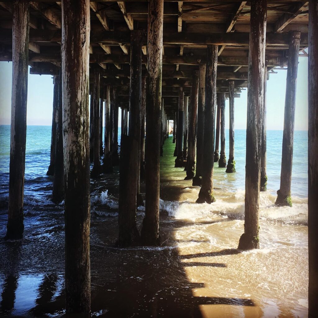 Album cover image of a photo taken under a pier at the ocean.